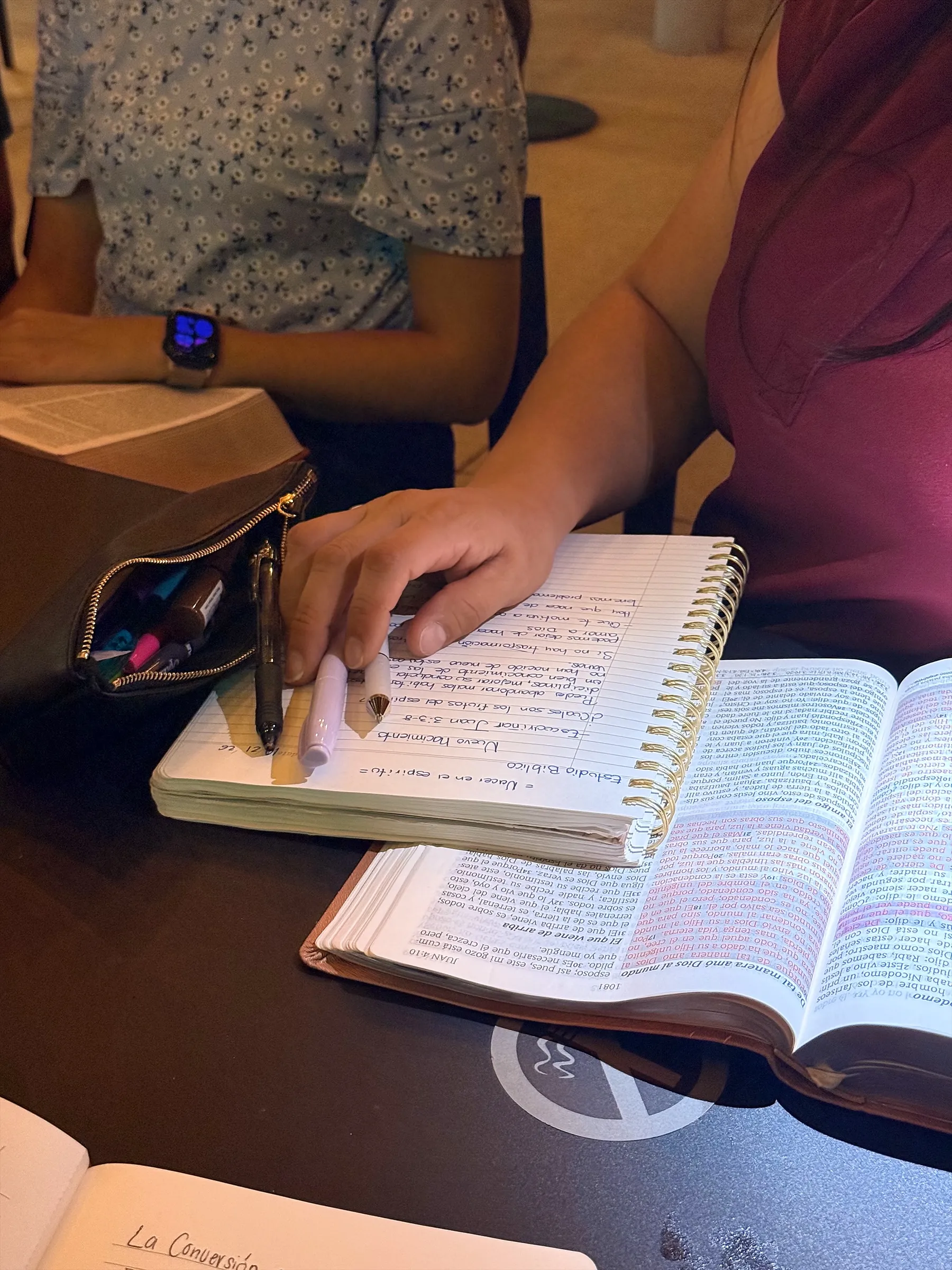 Manos tomando notas en una libreta junto a la Biblia abierta